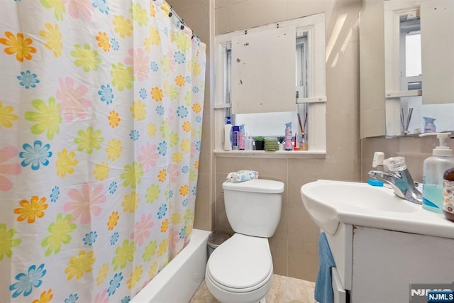 full bathroom featuring shower / bathtub combination with curtain, vanity, toilet, and tile walls