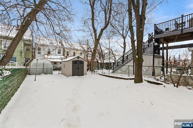 yard layered in snow with a wooden deck and a storage shed