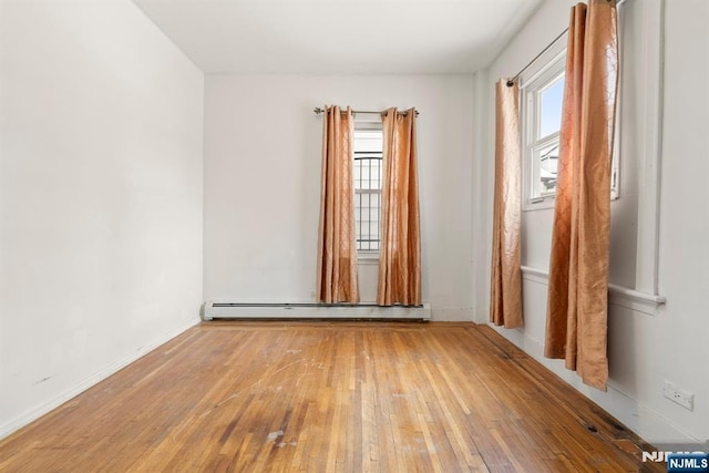 spare room featuring baseboard heating and light hardwood / wood-style floors