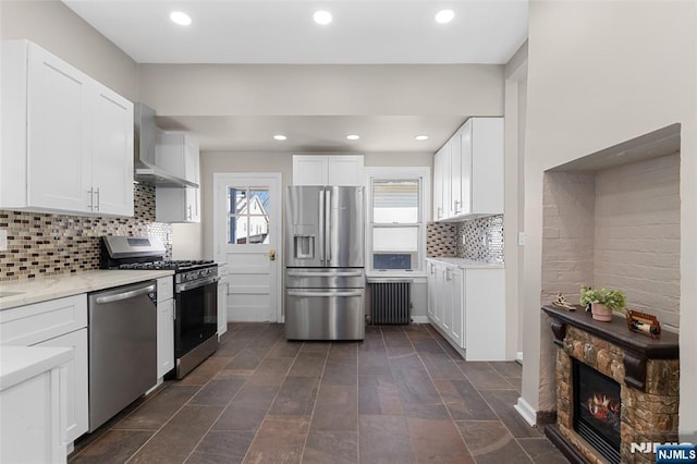 kitchen featuring appliances with stainless steel finishes, wall chimney exhaust hood, white cabinetry, and radiator heating unit