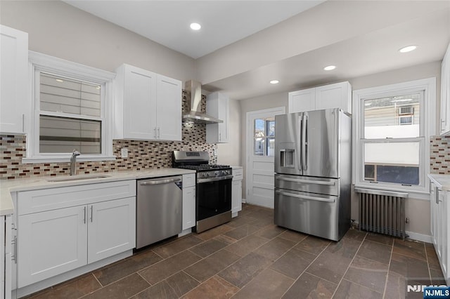 kitchen with appliances with stainless steel finishes, radiator heating unit, wall chimney exhaust hood, white cabinets, and sink