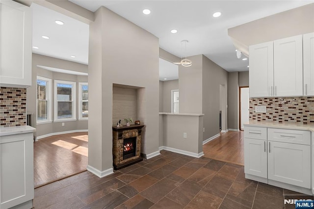 kitchen featuring a fireplace, tasteful backsplash, white cabinetry, and hanging light fixtures