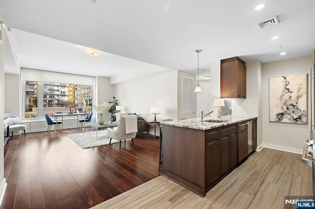 kitchen featuring visible vents, open floor plan, light wood-type flooring, stainless steel dishwasher, and a sink