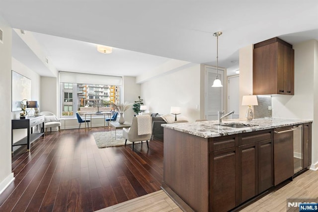 kitchen featuring wood finished floors, a sink, open floor plan, stainless steel dishwasher, and light stone countertops