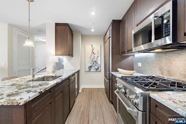 kitchen with light stone countertops, appliances with stainless steel finishes, dark brown cabinets, and a sink