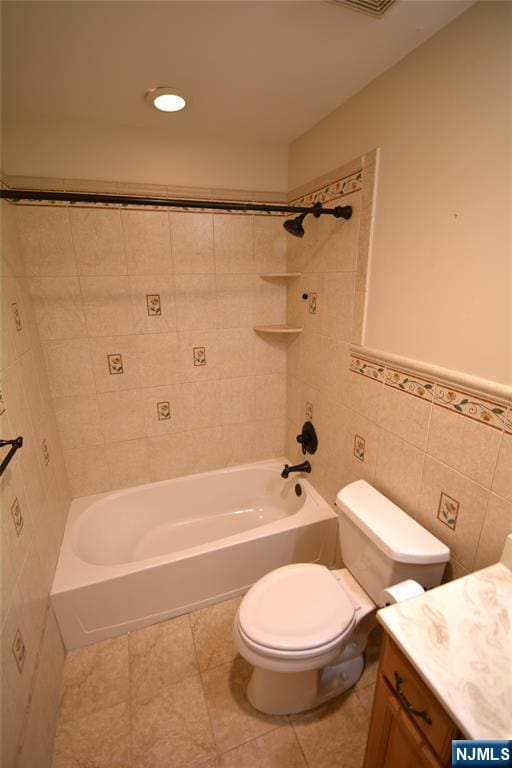 full bathroom featuring tile patterned flooring, tile walls, tiled shower / bath combo, vanity, and toilet