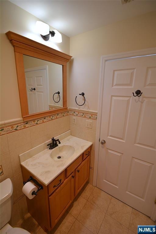 bathroom featuring tile patterned floors, vanity, toilet, and tile walls