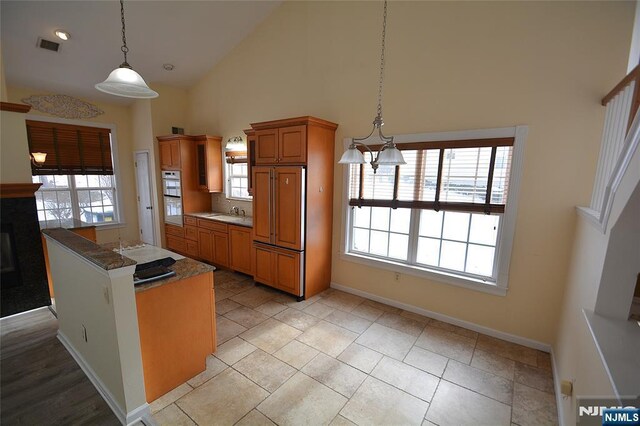 kitchen featuring high vaulted ceiling, double oven, sink, hanging light fixtures, and paneled refrigerator