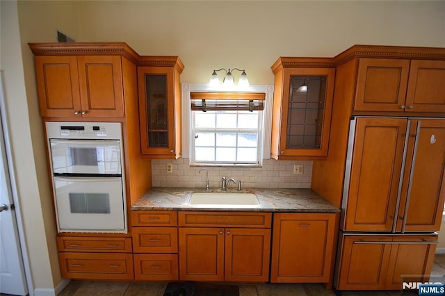 kitchen with sink, tasteful backsplash, high end refrigerator, double oven, and light stone countertops