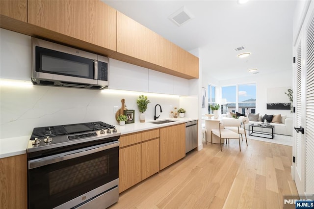 kitchen with appliances with stainless steel finishes, sink, decorative backsplash, light brown cabinets, and light wood-type flooring