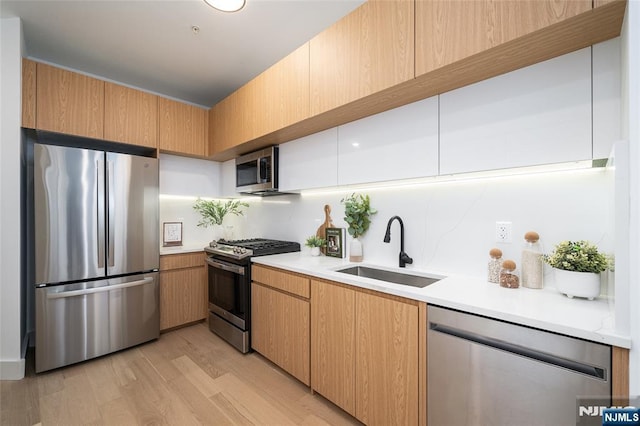 kitchen with appliances with stainless steel finishes, sink, and light hardwood / wood-style floors