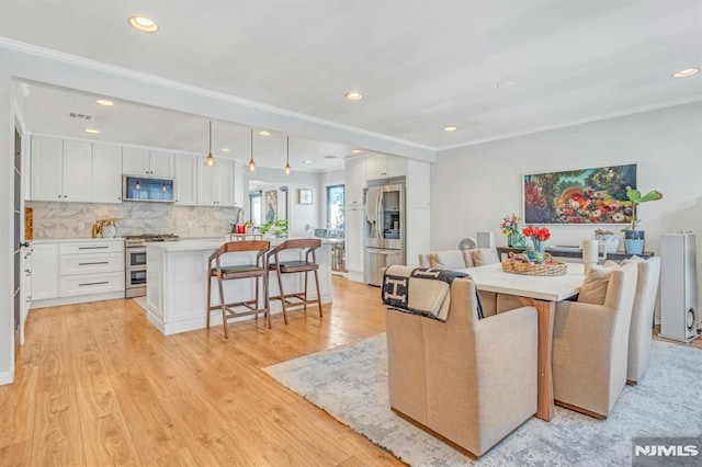 kitchen with decorative light fixtures, appliances with stainless steel finishes, a kitchen breakfast bar, a kitchen island, and white cabinets