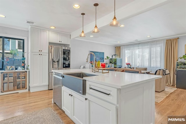 kitchen with white cabinetry, ornamental molding, a kitchen island with sink, stainless steel appliances, and light wood-type flooring