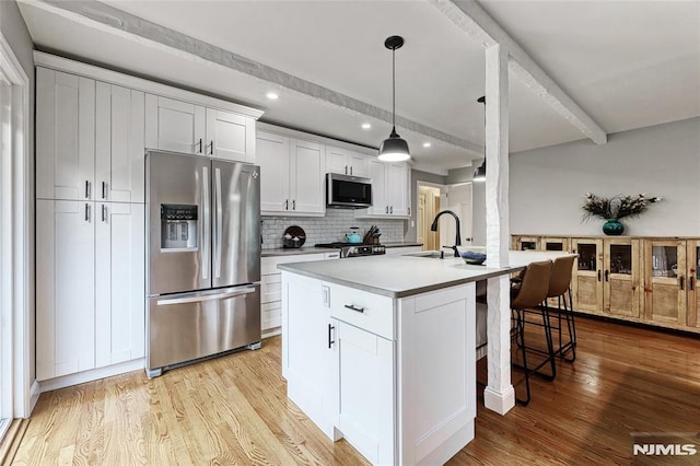 kitchen with sink, a center island with sink, hanging light fixtures, stainless steel appliances, and white cabinets