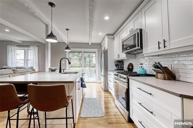 kitchen featuring sink, a breakfast bar area, appliances with stainless steel finishes, white cabinetry, and hanging light fixtures