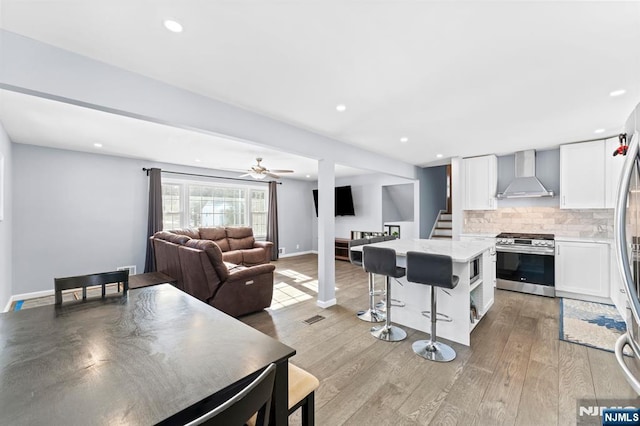 kitchen featuring a kitchen island, white cabinets, tasteful backsplash, appliances with stainless steel finishes, and wall chimney range hood