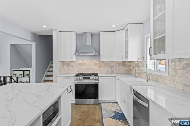 kitchen with white cabinetry, stainless steel appliances, sink, light stone counters, and wall chimney exhaust hood