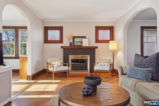 living room featuring wood-type flooring, a fireplace, ornamental molding, and baseboards