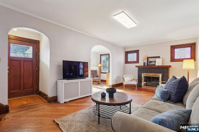 living room with a healthy amount of sunlight, a brick fireplace, arched walkways, and wood finished floors