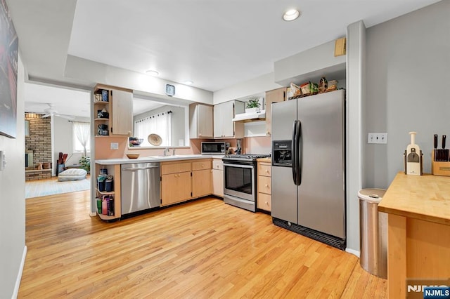 kitchen with sink, light hardwood / wood-style flooring, ceiling fan, appliances with stainless steel finishes, and a brick fireplace