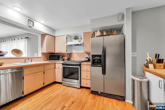 kitchen with stainless steel appliances, sink, light brown cabinetry, and light hardwood / wood-style floors