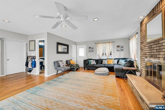 living room with ceiling fan, a brick fireplace, and light wood-type flooring