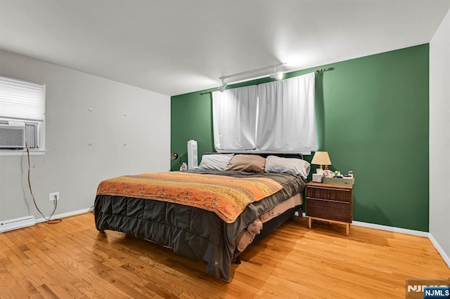 bedroom featuring cooling unit, hardwood / wood-style floors, and a baseboard heating unit