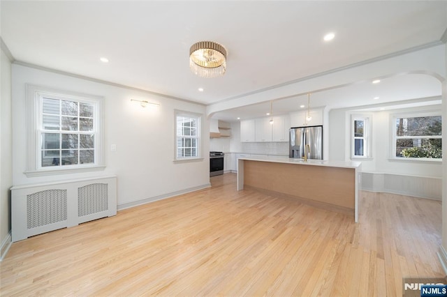 kitchen with a center island, hanging light fixtures, appliances with stainless steel finishes, radiator heating unit, and white cabinets