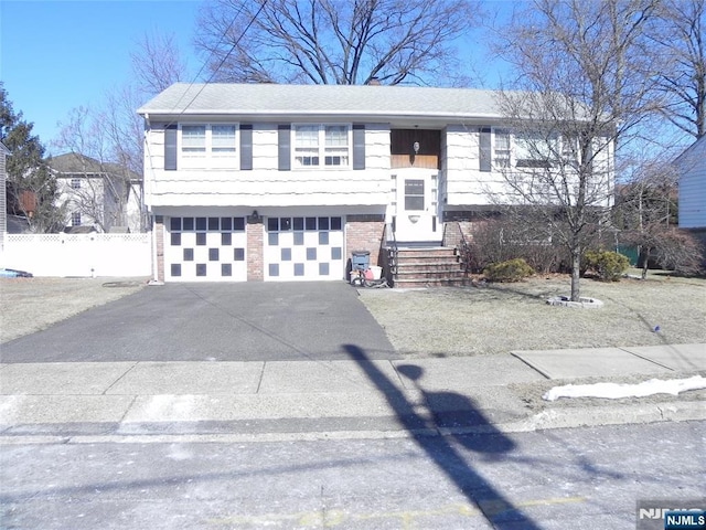 split foyer home featuring brick siding, a shingled roof, fence, a garage, and driveway