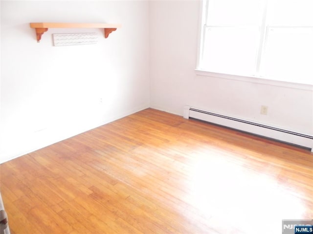 spare room featuring a baseboard heating unit and wood finished floors