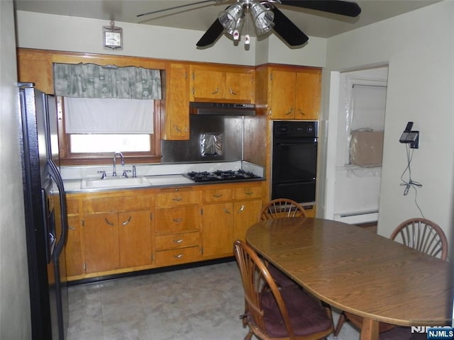 kitchen with black appliances, a sink, under cabinet range hood, brown cabinetry, and baseboard heating