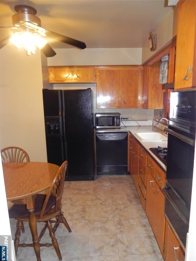 kitchen featuring brown cabinets, black appliances, a warming drawer, a ceiling fan, and a sink