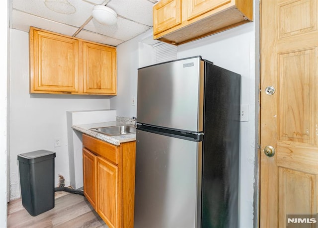 kitchen with stainless steel refrigerator, a paneled ceiling, sink, and light hardwood / wood-style flooring