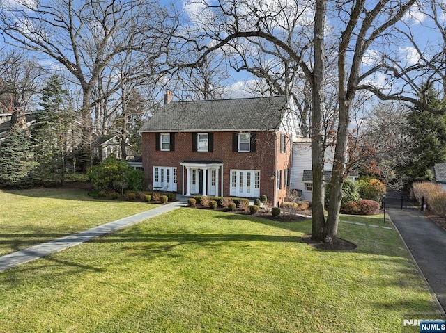 view of front facade featuring a chimney, a front lawn, and brick siding