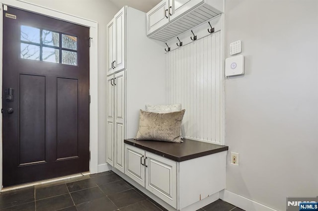 mudroom with dark tile patterned floors and baseboards