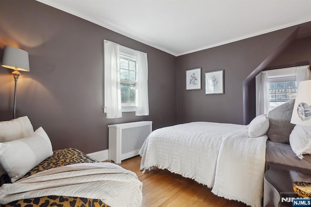 bedroom featuring radiator, multiple windows, crown molding, and wood finished floors