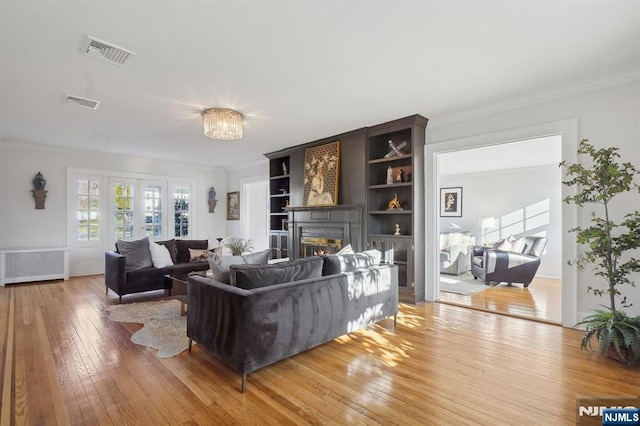 living room with ornamental molding, radiator heating unit, wood finished floors, and visible vents