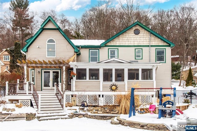 snow covered rear of property with a pergola and a sunroom