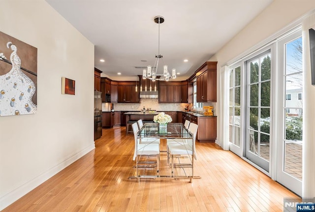 dining space featuring sink, light wood-type flooring, and a notable chandelier