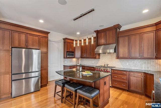 kitchen featuring appliances with stainless steel finishes, pendant lighting, a breakfast bar area, dark stone counters, and a center island with sink