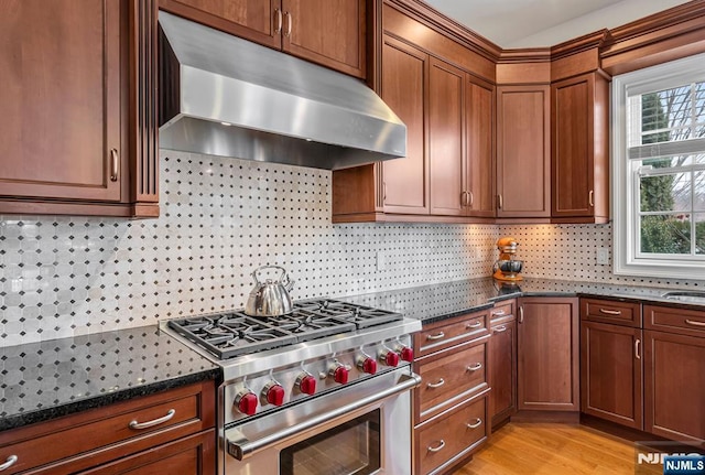 kitchen featuring high end stainless steel range oven, dark stone counters, decorative backsplash, and exhaust hood