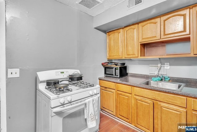 kitchen featuring white range with gas cooktop, sink, and light wood-type flooring