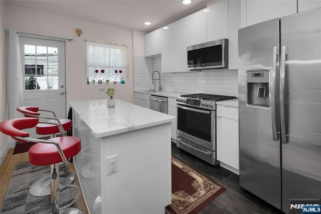 kitchen featuring sink, white cabinetry, backsplash, stainless steel appliances, and a kitchen island