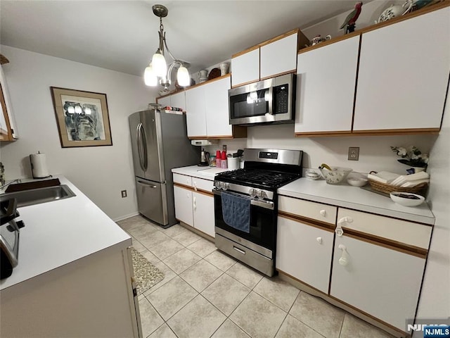 kitchen with light tile patterned flooring, appliances with stainless steel finishes, white cabinetry, sink, and hanging light fixtures