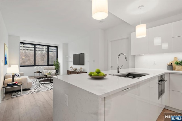 kitchen with sink, white cabinetry, decorative light fixtures, kitchen peninsula, and light wood-type flooring