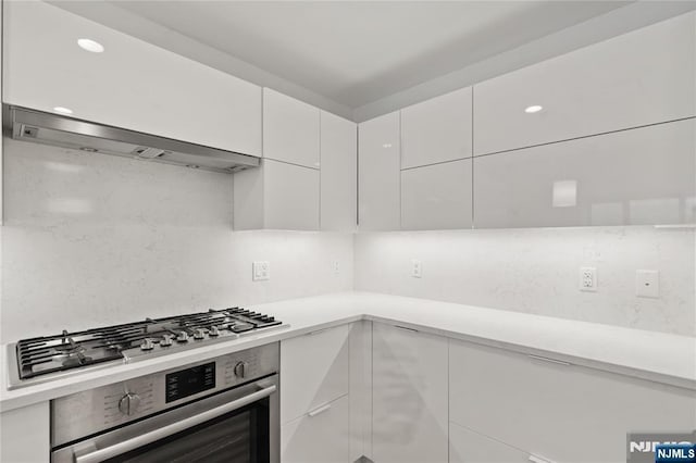 kitchen featuring white cabinetry, appliances with stainless steel finishes, backsplash, and wall chimney range hood