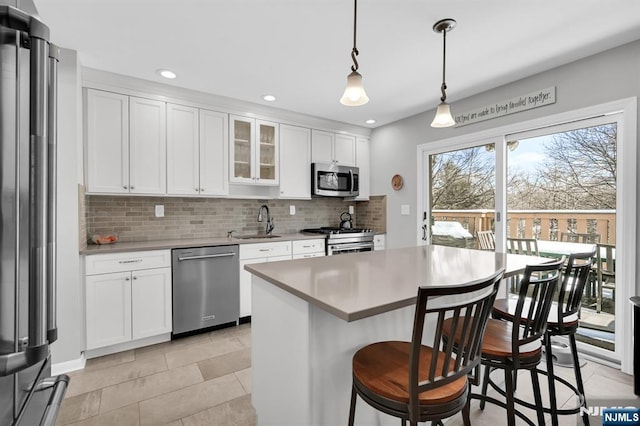 kitchen with appliances with stainless steel finishes, decorative light fixtures, sink, white cabinets, and a center island