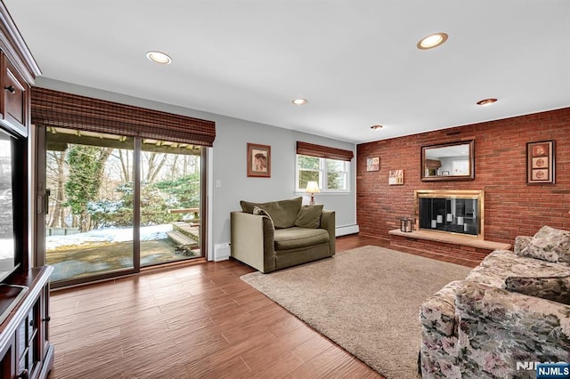 living room featuring hardwood / wood-style flooring, brick wall, a fireplace, and baseboard heating