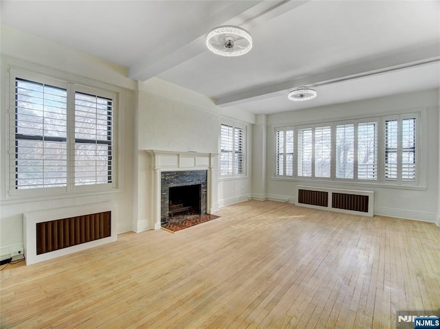 unfurnished living room with beamed ceiling, radiator heating unit, a fireplace, and light wood-type flooring