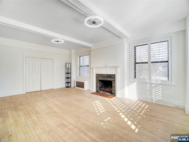 unfurnished living room with a premium fireplace, beam ceiling, and light hardwood / wood-style flooring